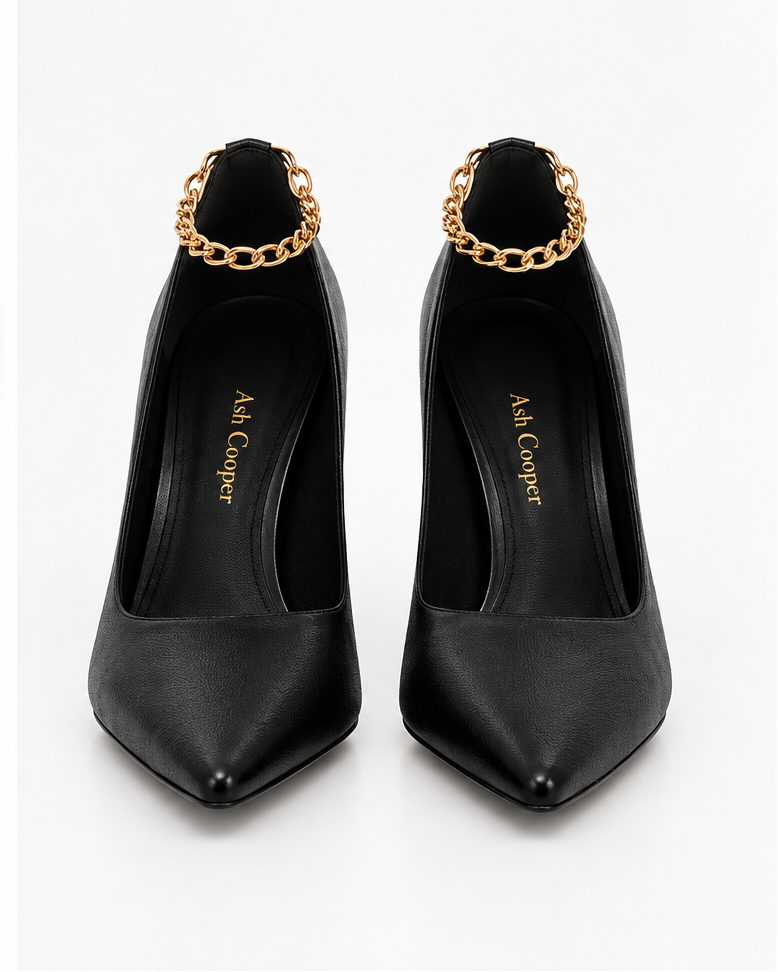 The Chain Pump by Ash Cooper: a pair of black pointed-toe leather pumps with gold-tone ankle chains, front view